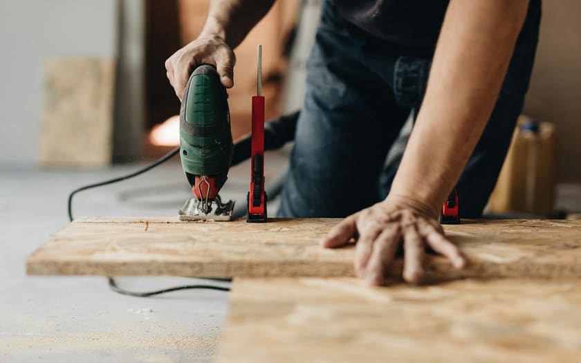 Handwerker sägt mit einer Stichsäge eine Holzplatte auf einer Werkbank zu.